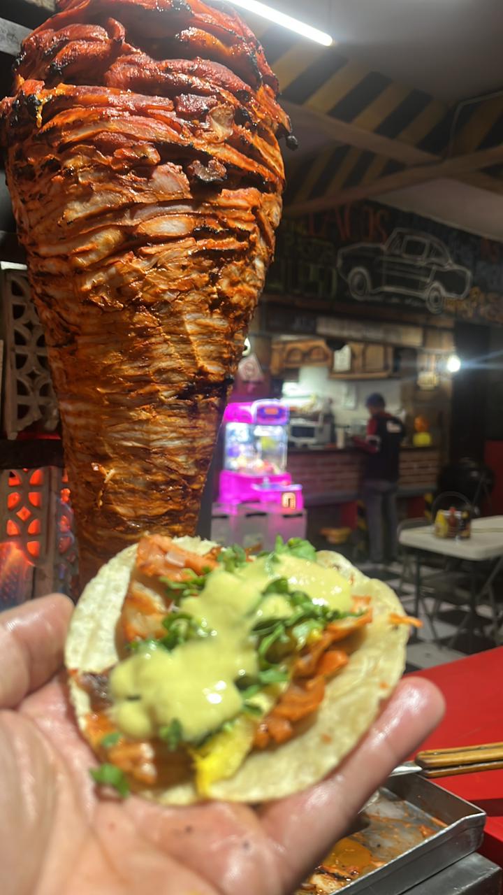 Taco al pastor de El Tacómetro con trompo al fondo